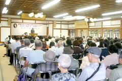 写真 挨拶する木島日出夫伊藤千代子没後80年記念のつどい代表 会場にはいっぱいの人人々・・・
