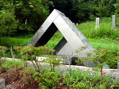 写真　緑に囲まれてたつ三角形の顕彰碑（石碑）